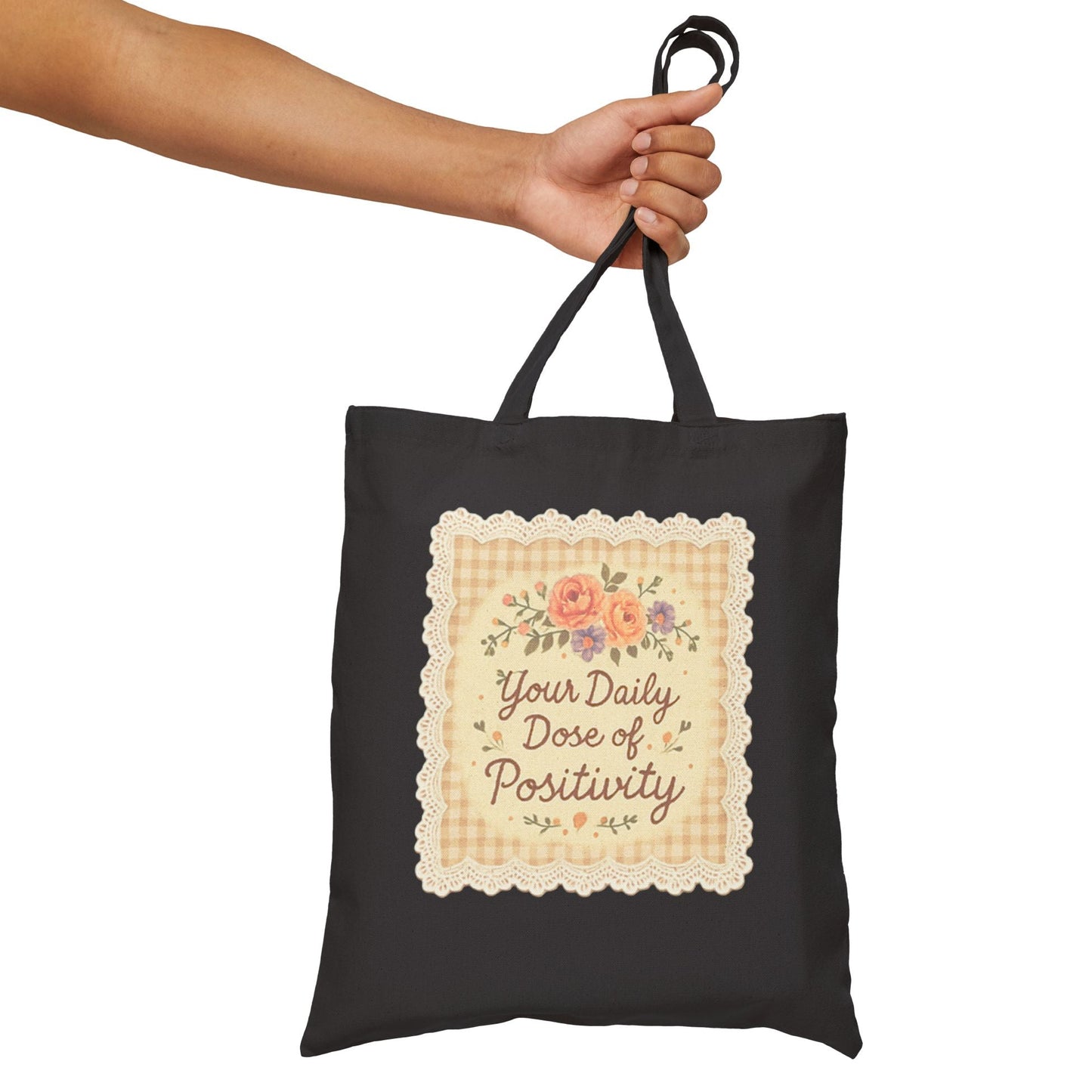 Black tote bag with floral design and text held by a hand on a white background