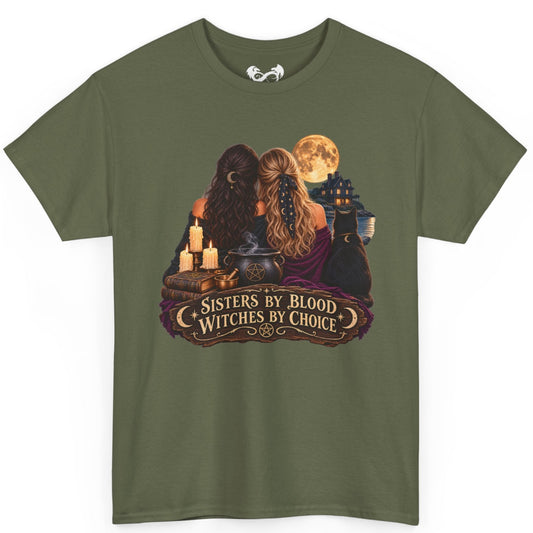 An olive green short-sleeve t-shirt with a graphic print of two witches sitting together under a full moon, featuring candles, a cauldron, and a banner that reads 'Sisters by Blood Witches by Choice'.