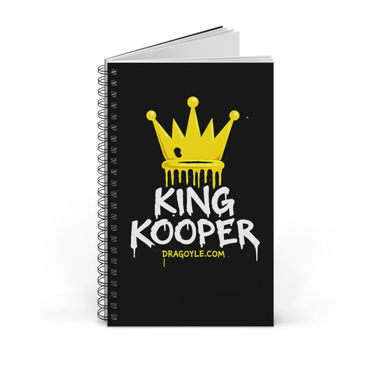 A black spiral-bound notebook standing upright on a white background. The cover features a yellow dripping crown graphic above the text 'KING KOOPER' in white and 'DRAGOYLE.