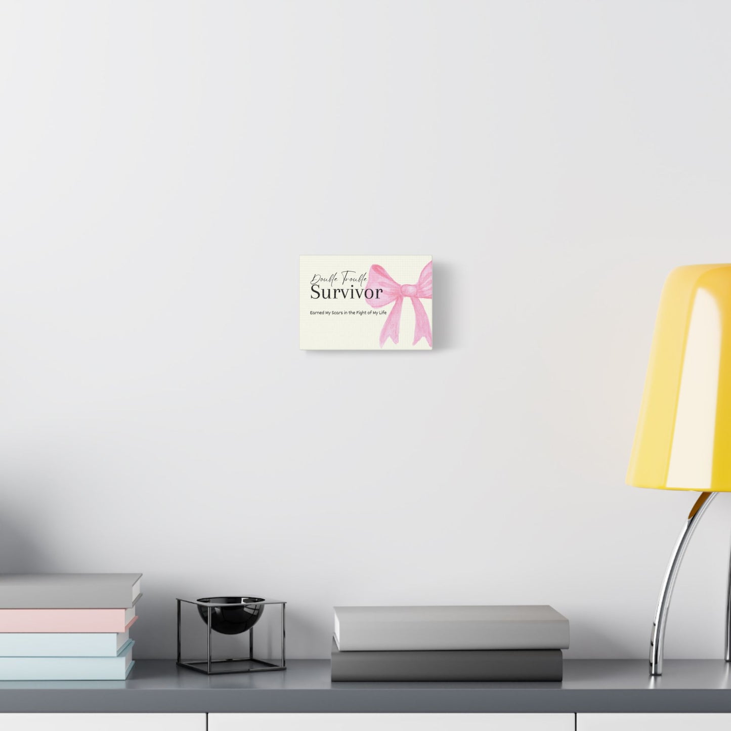 Decorative wall art with a pink ribbon and text on a white wall above a shelf.