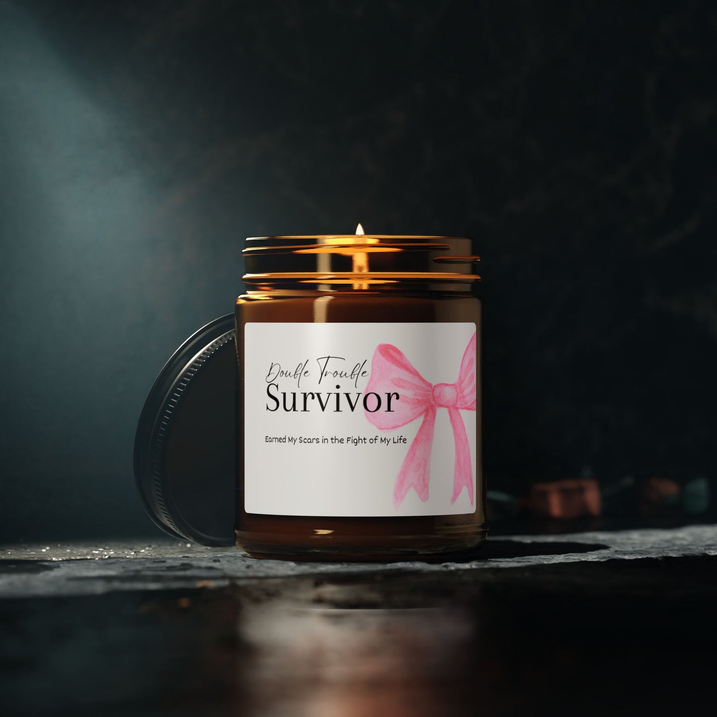 Candle in a jar with a label reading 'Survivor' and a pink ribbon on a dark background.