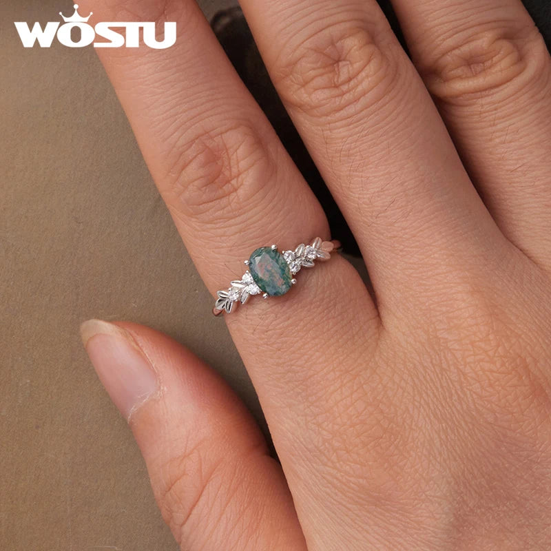 Ring with a green gemstone on a finger, branded 'WOSTU'.