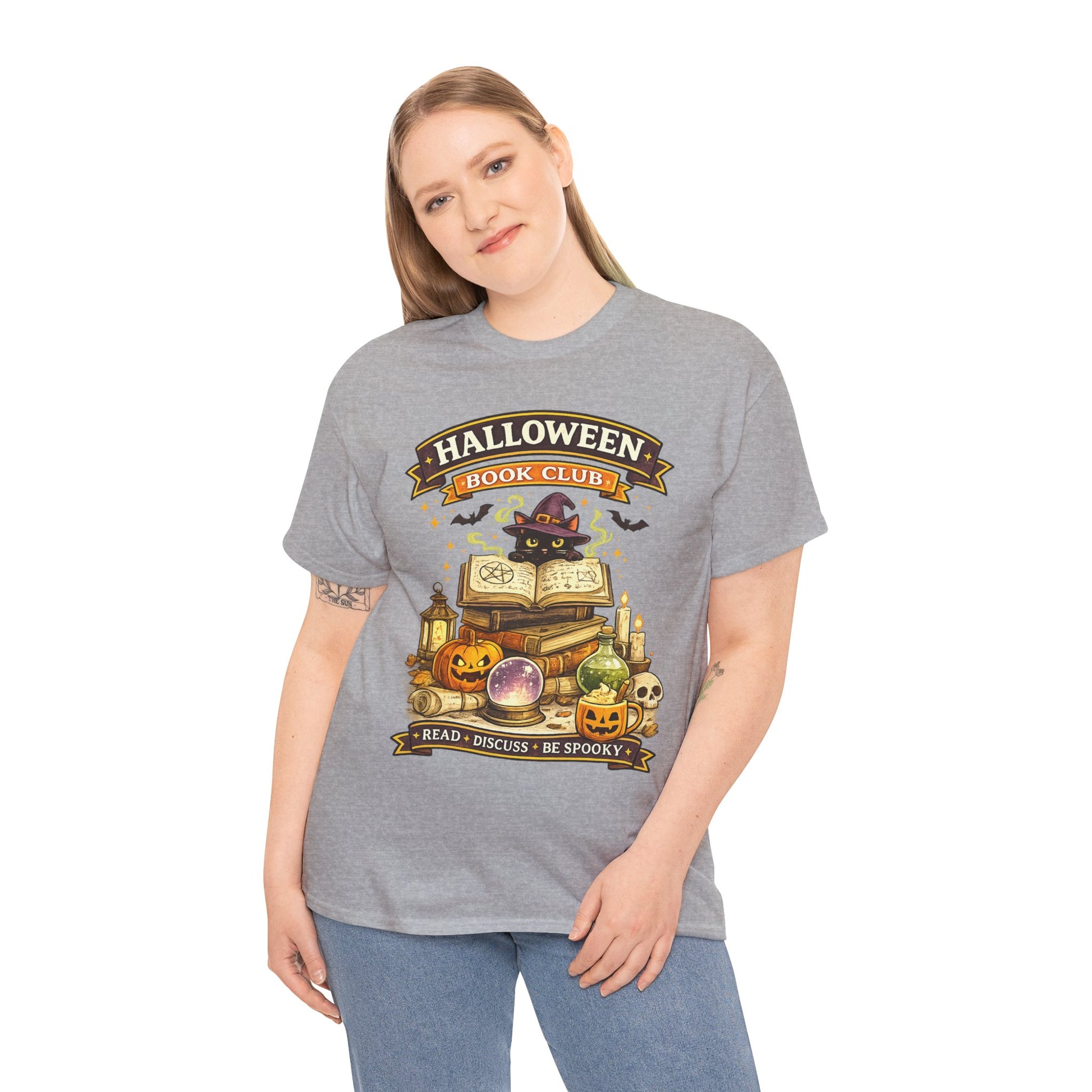 A woman modeling a heather gray graphic t-shirt with a 'Halloween Hook Club' design featuring an open book, potion bottles, a skull, and a witch on a broom, paired with blue jeans against a white background.