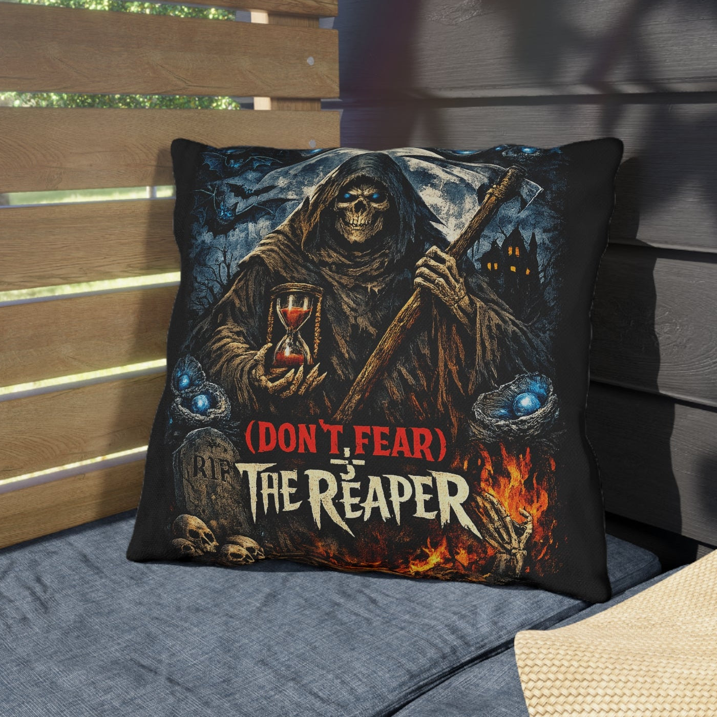 A square throw pillow featuring a grim reaper graphic with the text '(DON'T FEAR) THE REAPER' in red and white, styled on a blue patio cushion next to a straw hat.