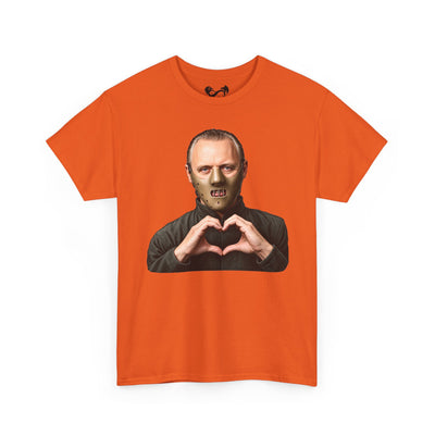 An orange short-sleeve crewneck t-shirt featuring a graphic print of a man in a black turtleneck making a heart shape with his hands, set against a plain white background.