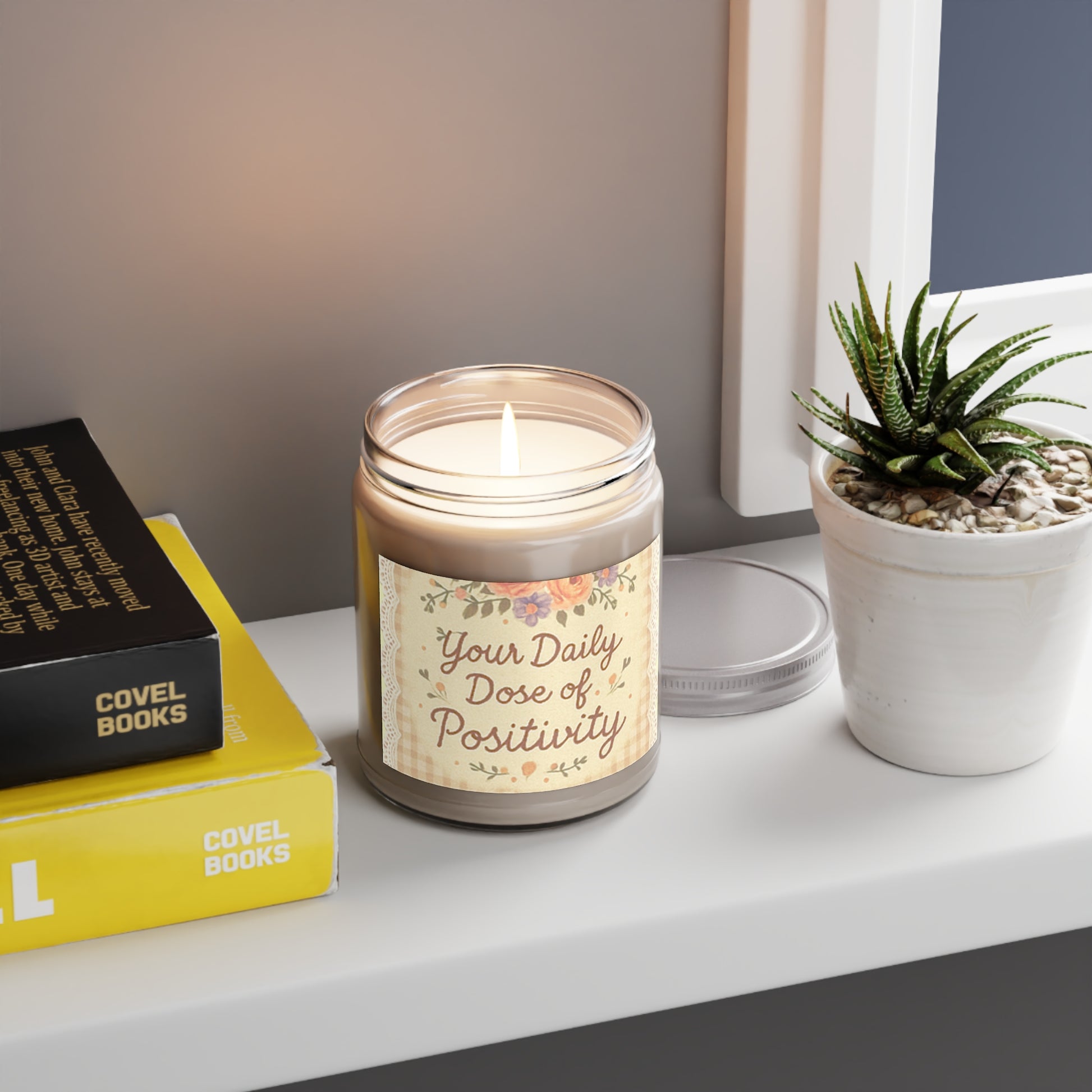 Candle labeled 'Your Daily Dose of Positivity' on a shelf with books and a plant.