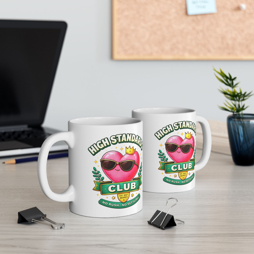 Two mugs with 'High Standards Club' design on a desk with office supplies.