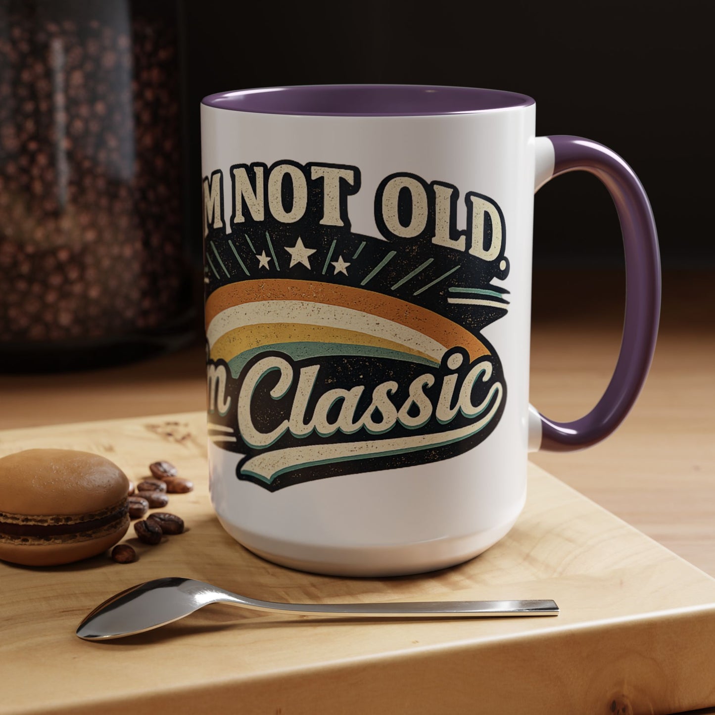 White mug with purple handle and text 'I'm not old, I'm classic' on a wooden surface with coffee beans and a spoon.