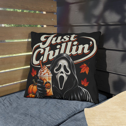 A square throw pillow with a Ghostface 'Just Chillin'' graphic, styled on a blue outdoor patio cushion next to a straw hat.