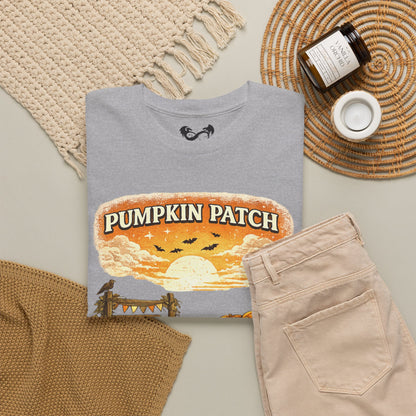 A folded light gray T-shirt with a large 'Pumpkin Patch' autumn graphic print, styled in a flat lay with beige pants, a woven blanket, a candle jar, and a small cup on a neutral background.