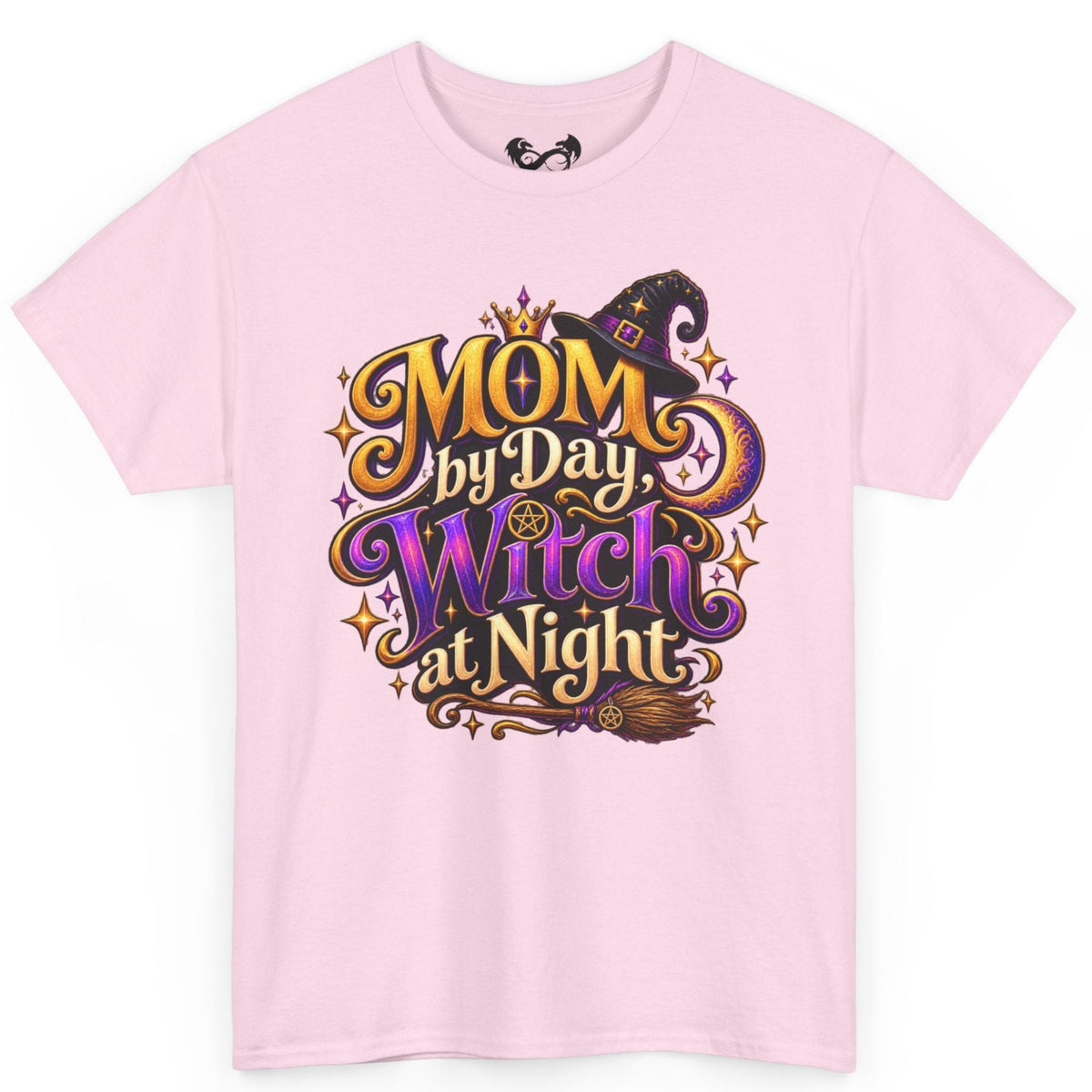 A light pink short-sleeve crewneck t-shirt featuring a colorful graphic on the front that reads 'MOM by Day, Witch at Night' in stylized gold, purple, and black lettering with a witch hat and broomstick illustration.