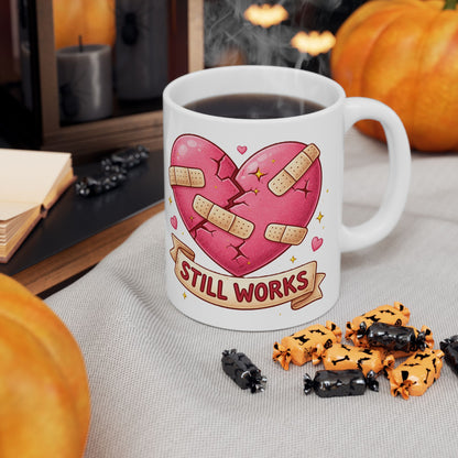 Mug with a heart design and 'Still Works' text, surrounded by Halloween-themed treats on a table.