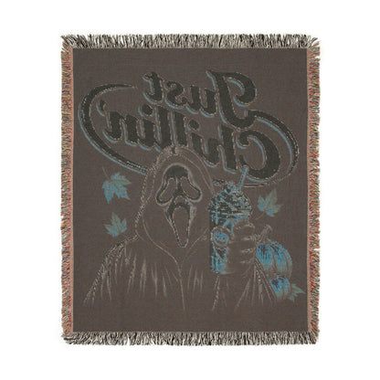 A dark brown woven throw blanket with fringe on all sides, featuring a graphic design with a deer head, blue leaves, and stylized text reading 'Chillin' Just'.