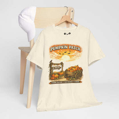 An off-white graphic t-shirt on a wooden hanger, styled in front of a light wood chair with a white cap. The t-shirt features a 'Pumpkin Patch' autumn graphic with pumpkins in a cart, a sun, and birds.