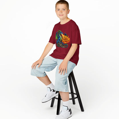 A boy sitting on a black stool wearing a maroon t-shirt with a colorful graphic print, light blue denim shorts, white socks, and white sneakers, photographed against a seamless white background.