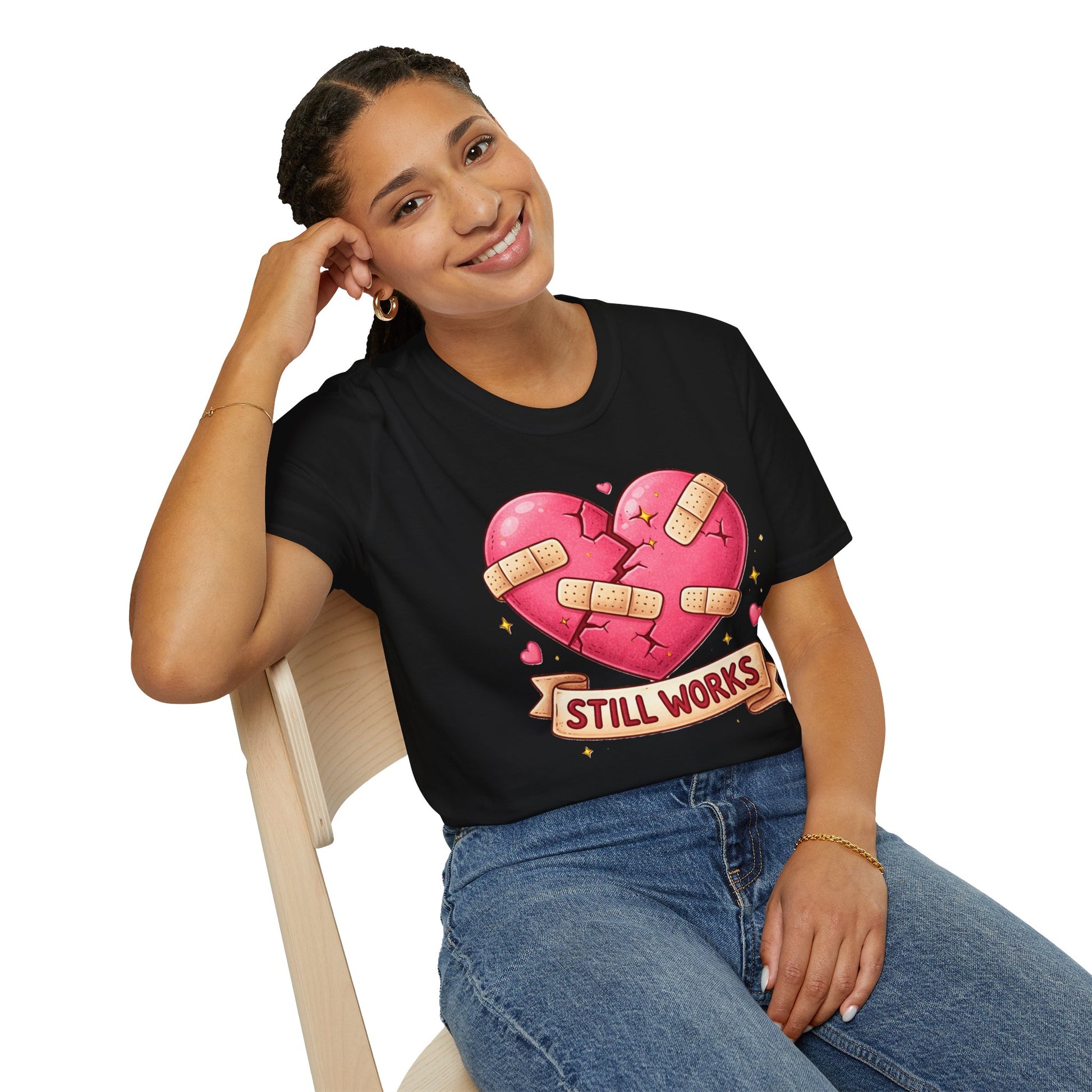 Person wearing a black t-shirt with a pink heart graphic and 'STILL WORKS' text, sitting on a chair.
