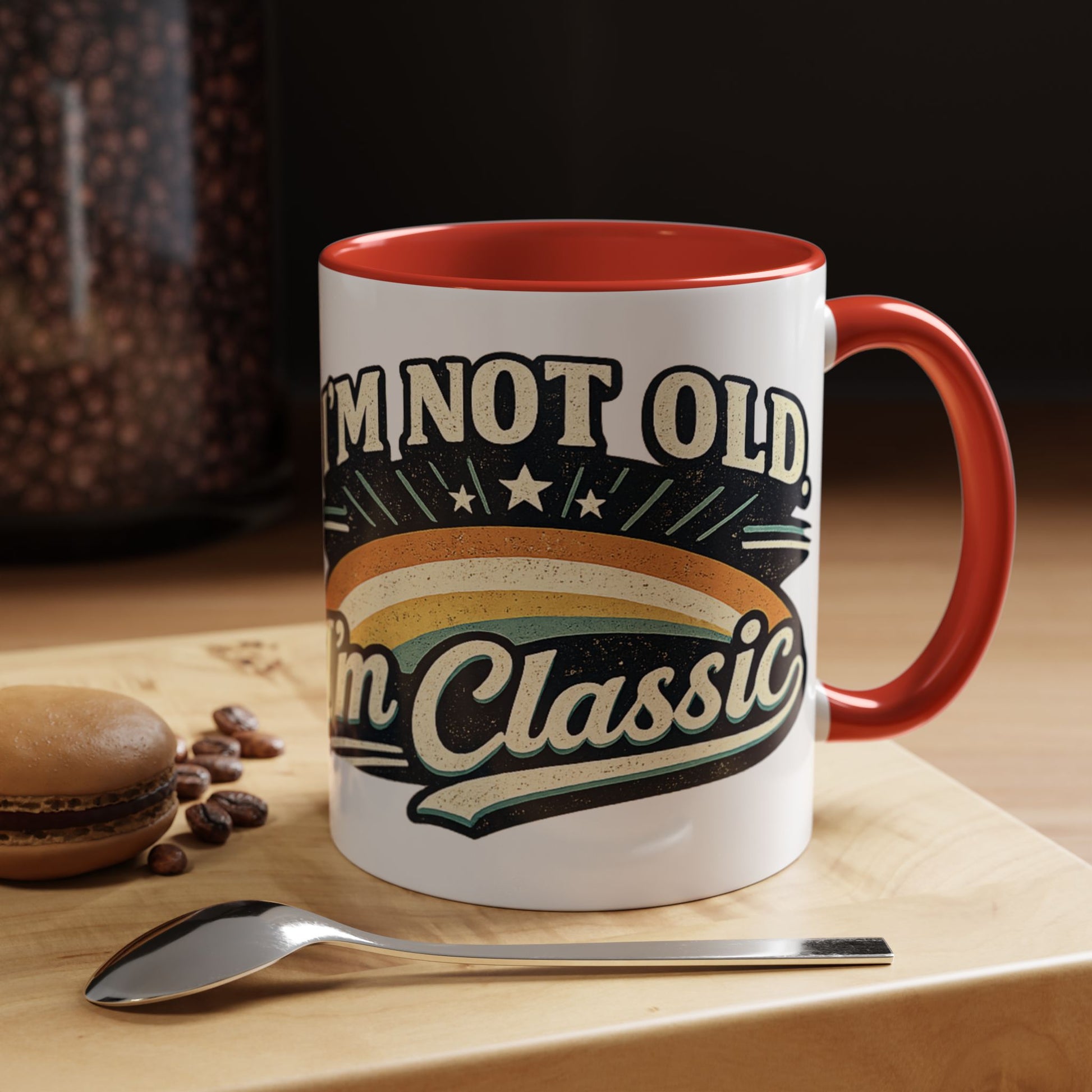 White mug with red interior and handle, featuring 'I'm not old, I'm classic' text, on a wooden surface with coffee beans and a spoon.