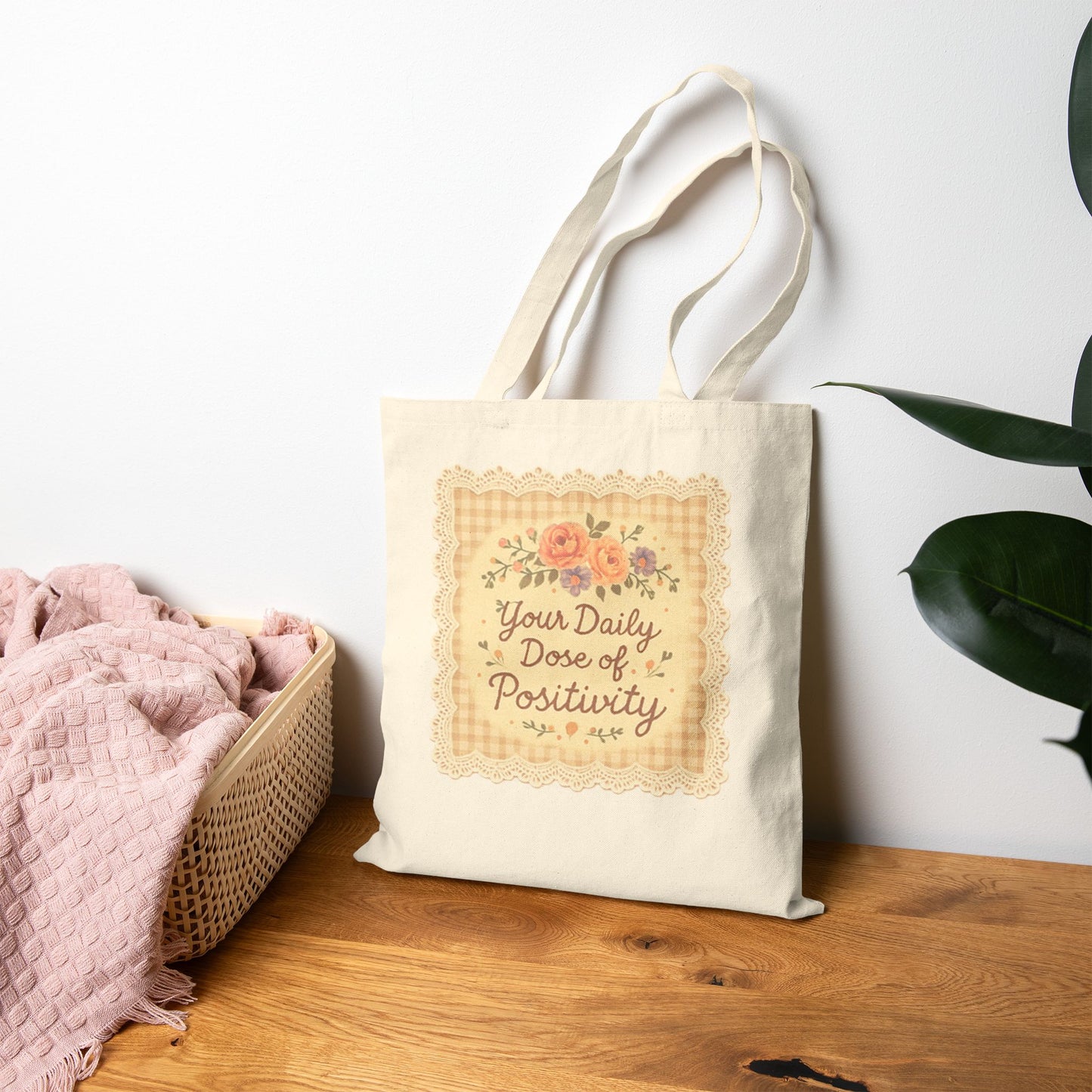 Tote bag with 'Your Daily Dose of Positivity' text on a wooden surface with a plant in the background
