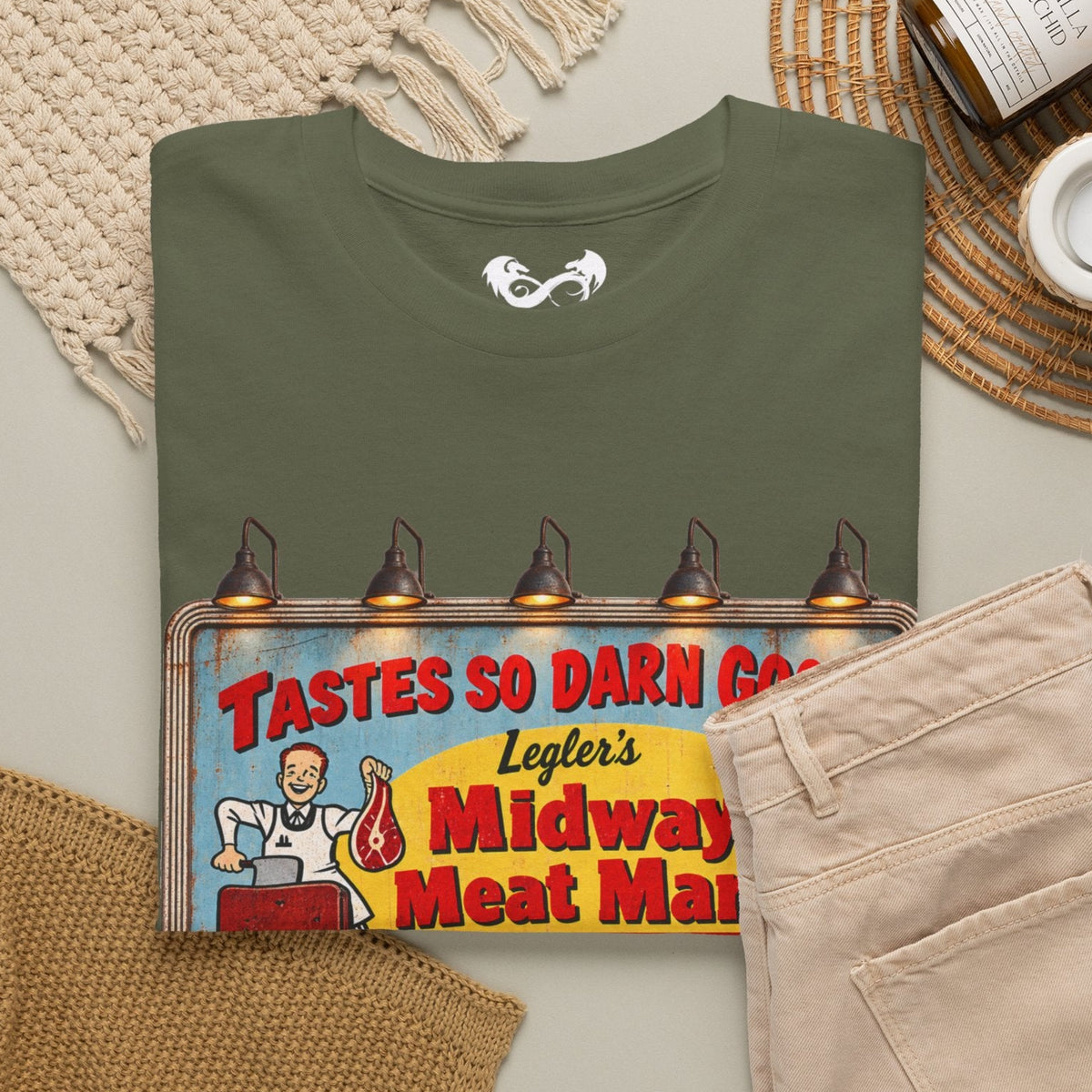 Bring a little vintage roadside horror to your wardrobe with this Jeepers Creepers-inspired Midway Meat Market T-shirt. Featuring the unmistakable retro roadside billboard design, distressed colors, bold red lettering, and classic old-school butcher-shop artwork, this shirt has the perfect mix of creepy, nostalgic, and Americana charm.