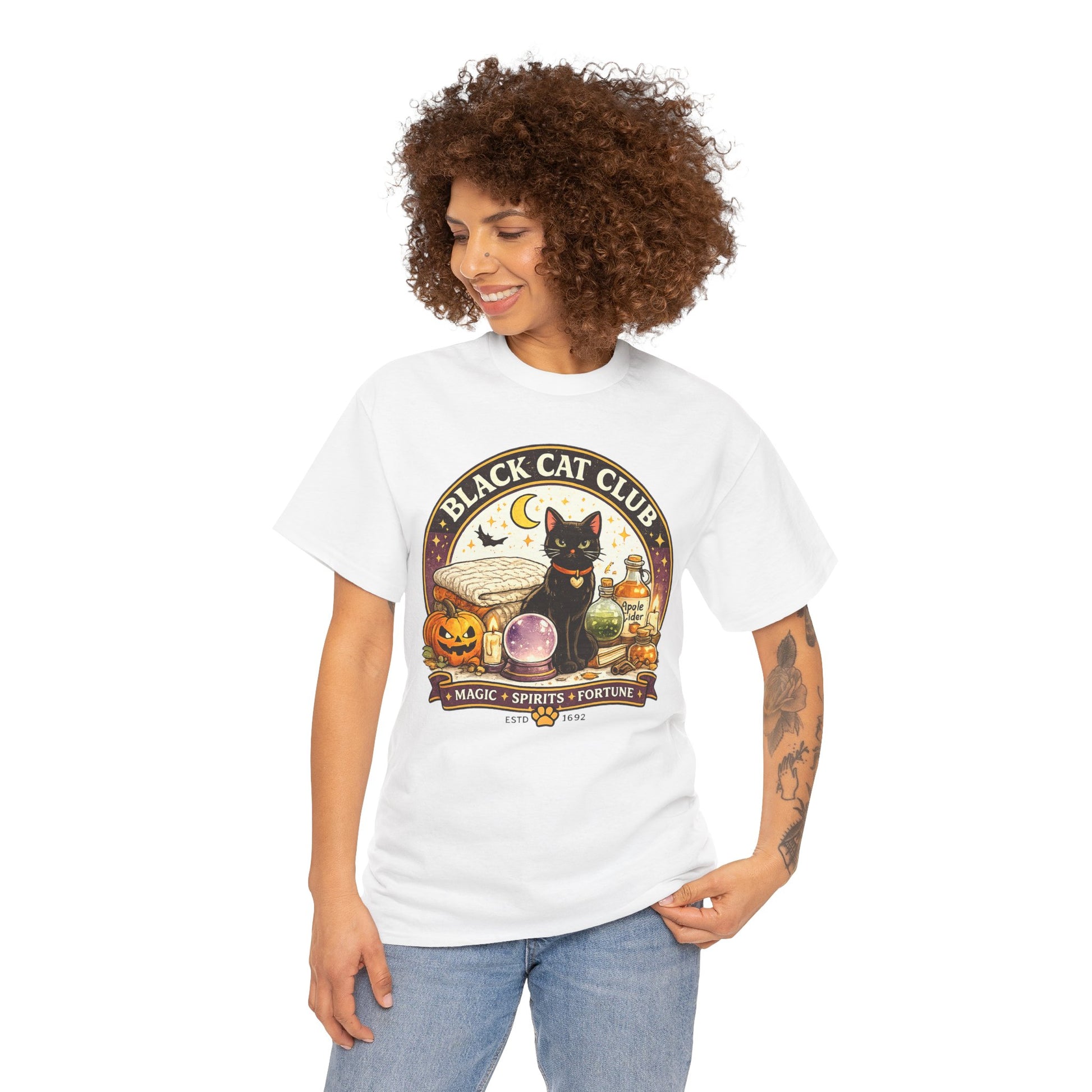 A woman with curly brown hair wearing a white graphic t-shirt and light blue jeans, shown from the waist up against a plain white background. The t-shirt features a circular 'Black Cat Club' graphic with a black cat, a jack-o'-lantern, a purple crystal ball, and a crescent moon.