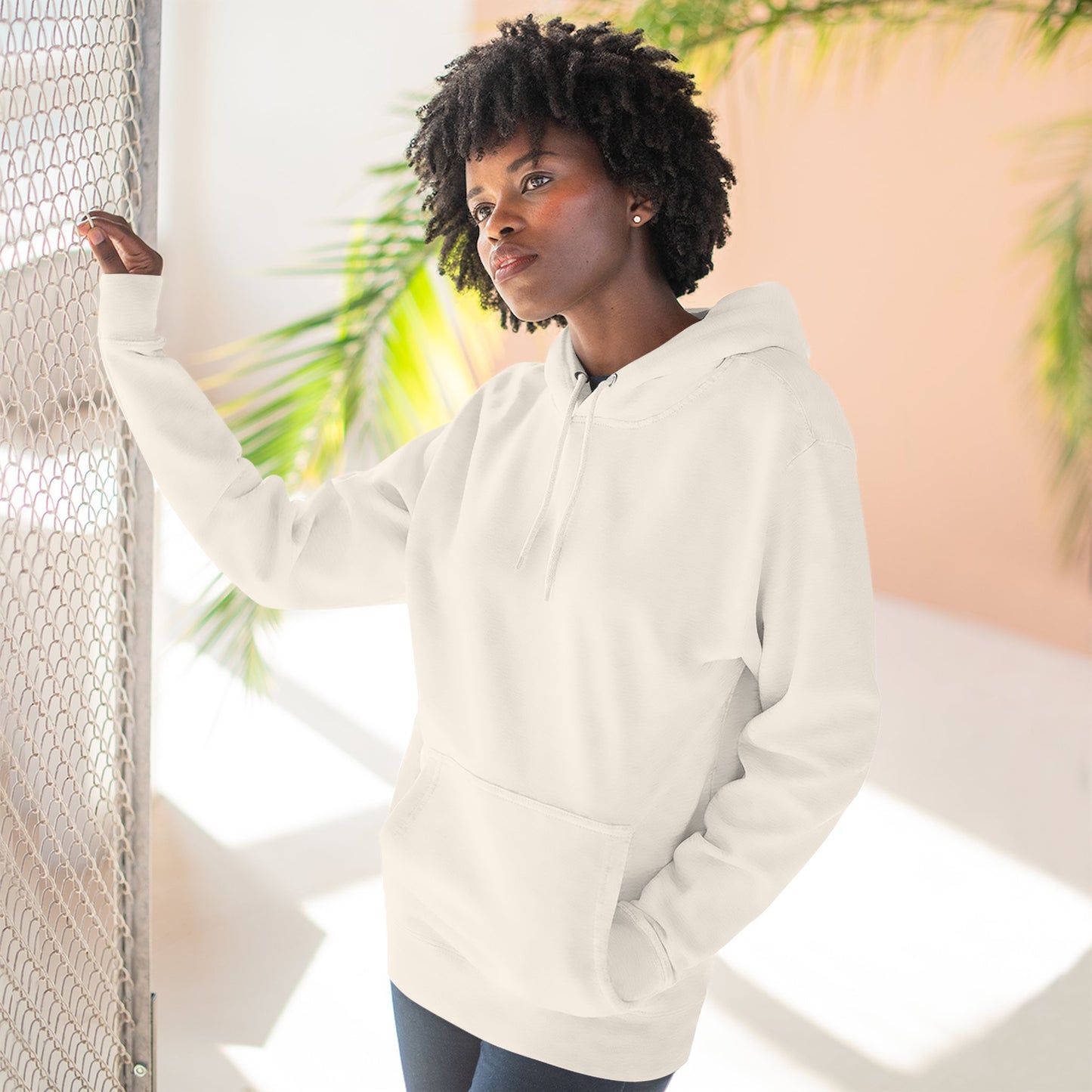 Person wearing a white hoodie standing against a light background with plants.
