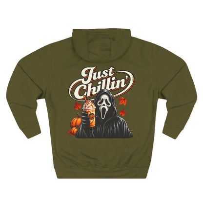 An olive green hoodie shown from the back, featuring a graphic print of the Ghostface character holding an iced coffee with pumpkin and autumn leaf accents, and the text 'Just Chillin'' in white and orange.
