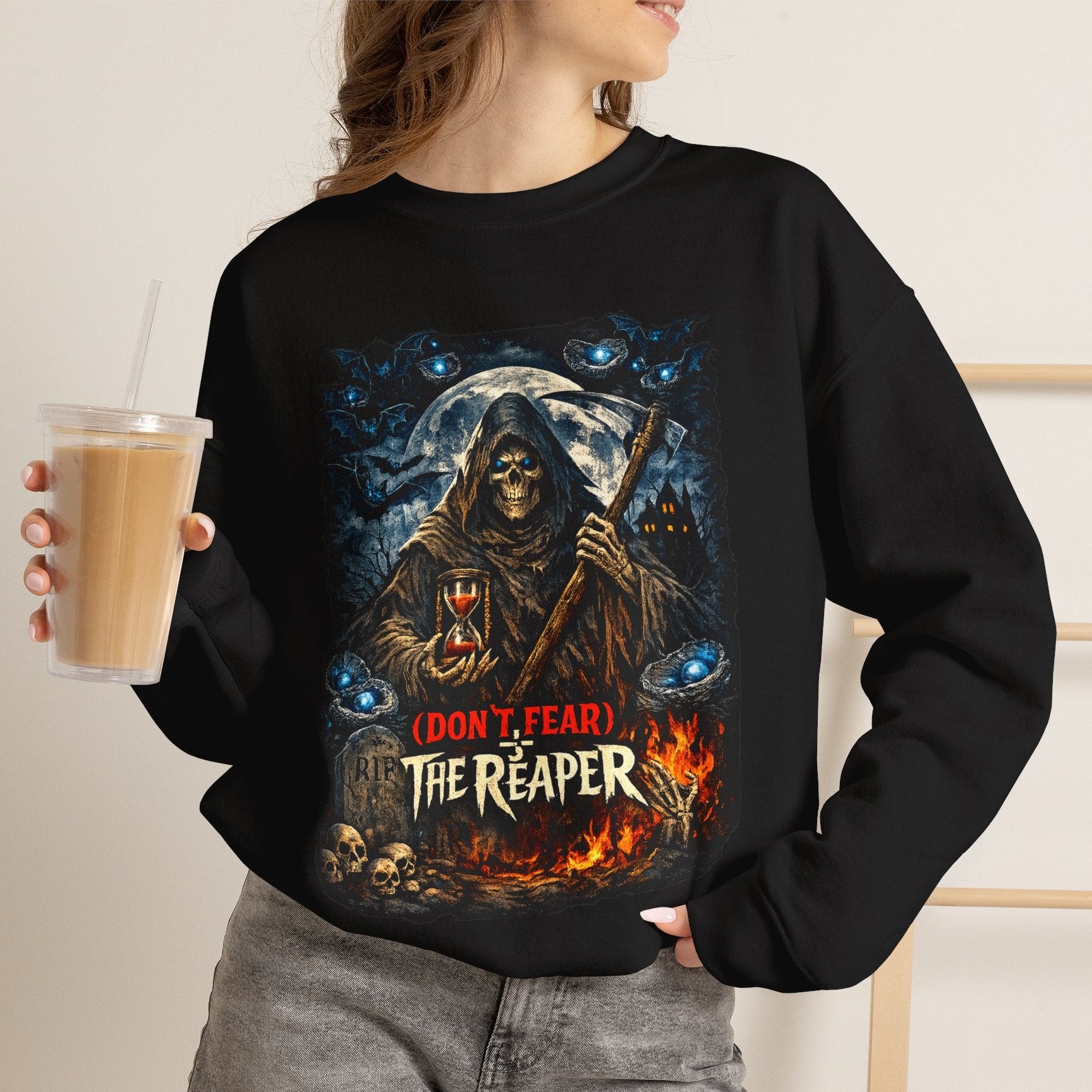 A woman wearing a black crewneck sweatshirt with a detailed graphic of the Grim Reaper holding a scythe in front of a moonlit sky with blue eyes. The graphic includes the text '(DON'T FEAR) THE REAPER' in red and white.
