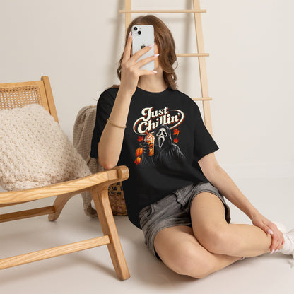 Person wearing a black t-shirt with text, sitting on the floor with a phone in front of a wooden chair.