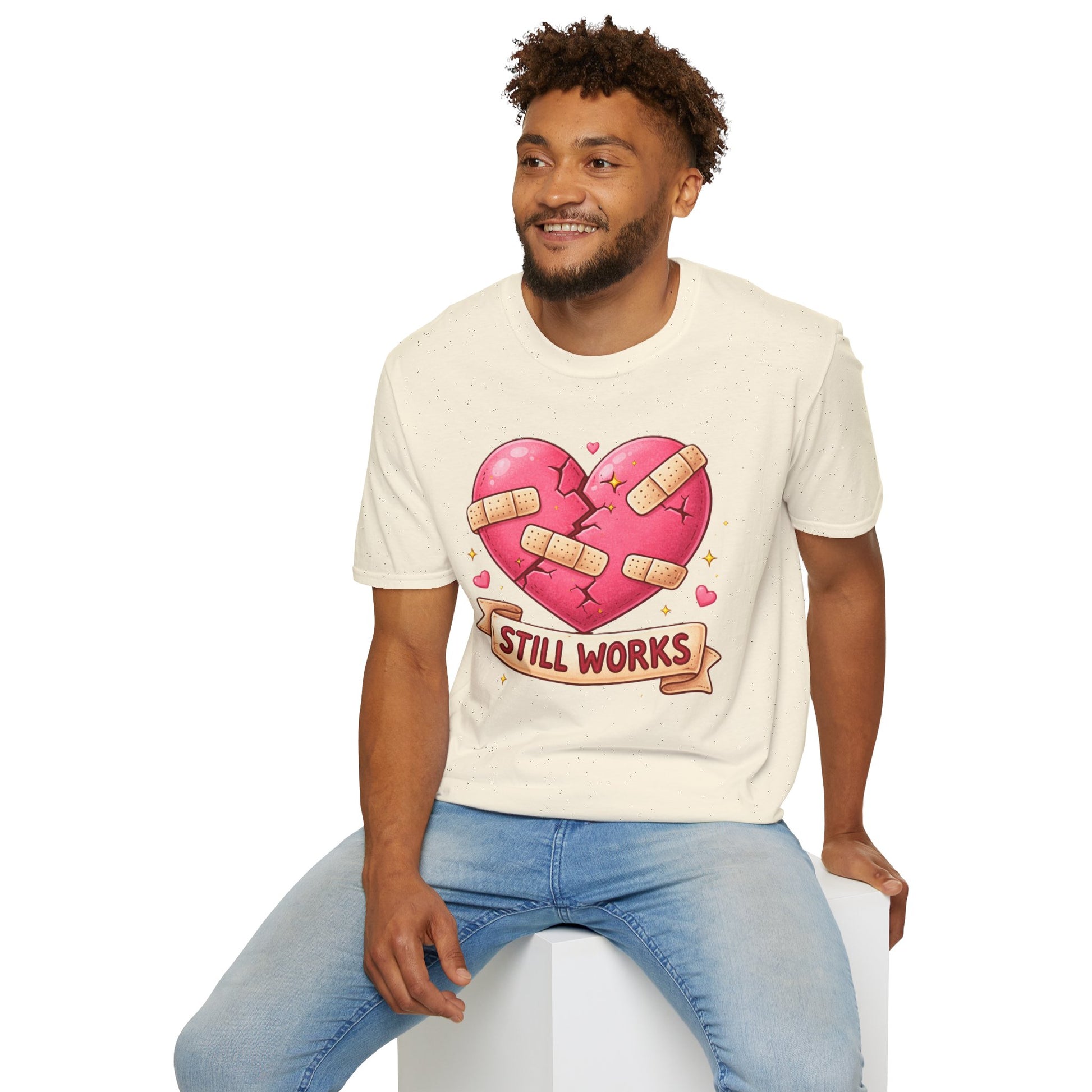 Man wearing a cream t-shirt with a heart design and text, sitting on a white stool against a white background.