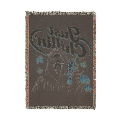 A rectangular woven throw blanket with fringe on all sides, featuring a dark brown background and a large stylized graphic of a Native American head with blue and light blue leaf accents and the text 'Black Crow'.