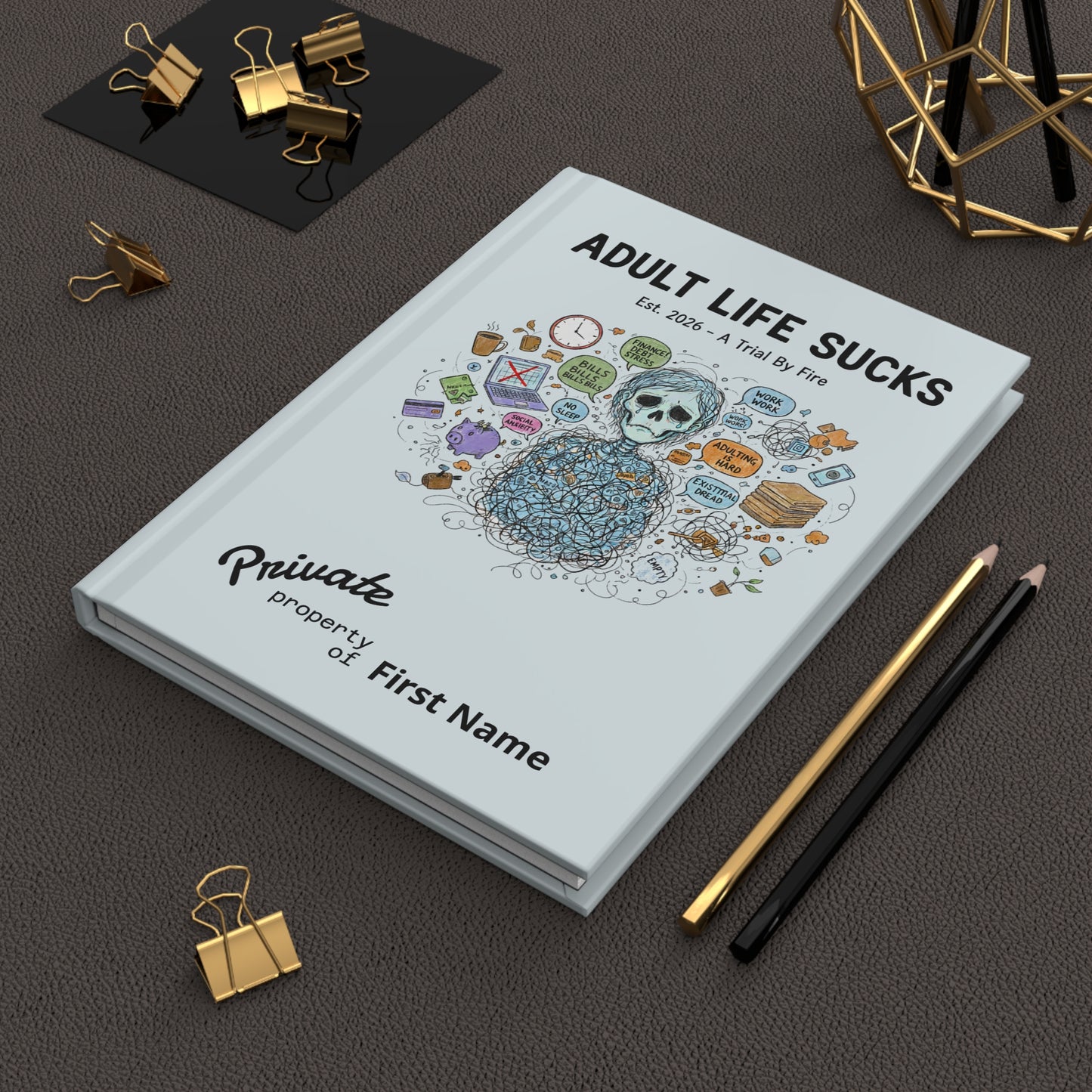 Notebook titled 'Adult Life Sucks' with decorative cover on a dark surface with office supplies.