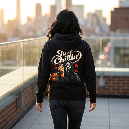A person viewed from behind wearing a black hoodie with a large Ghostface graphic and the words 'Just Chillin'' on the back, standing on a rooftop terrace at sunset.