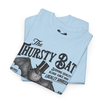A light blue folded t-shirt featuring a vintage-style black graphic of a bat wearing a top hat with the text 'The Thirsty Bat' and 'Serving quality blood, since 1689'.