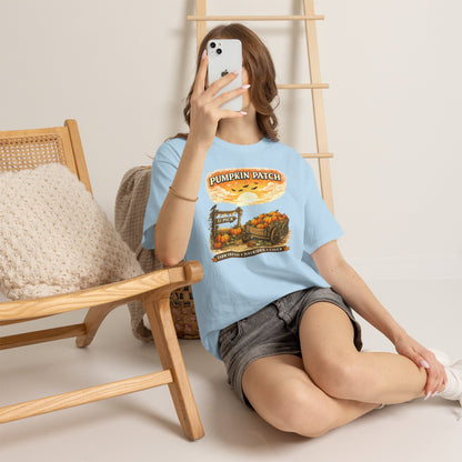 A woman takes a mirror selfie while wearing a light blue graphic t-shirt that reads 'PUMPKIN PATCH' with a pumpkin illustration, paired with gray denim shorts, sitting on a white floor next to a wooden chair.
