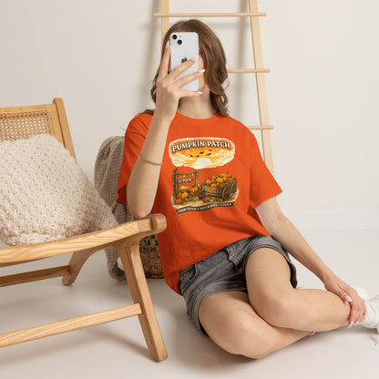 A woman takes a mirror selfie while wearing a bright orange graphic t-shirt that reads 'PUMPKIN PATCH' with a pumpkin illustration, paired with gray denim shorts in a cozy indoor setting.
