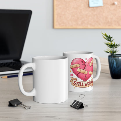 Two mugs on a desk with one featuring a heart design and text.