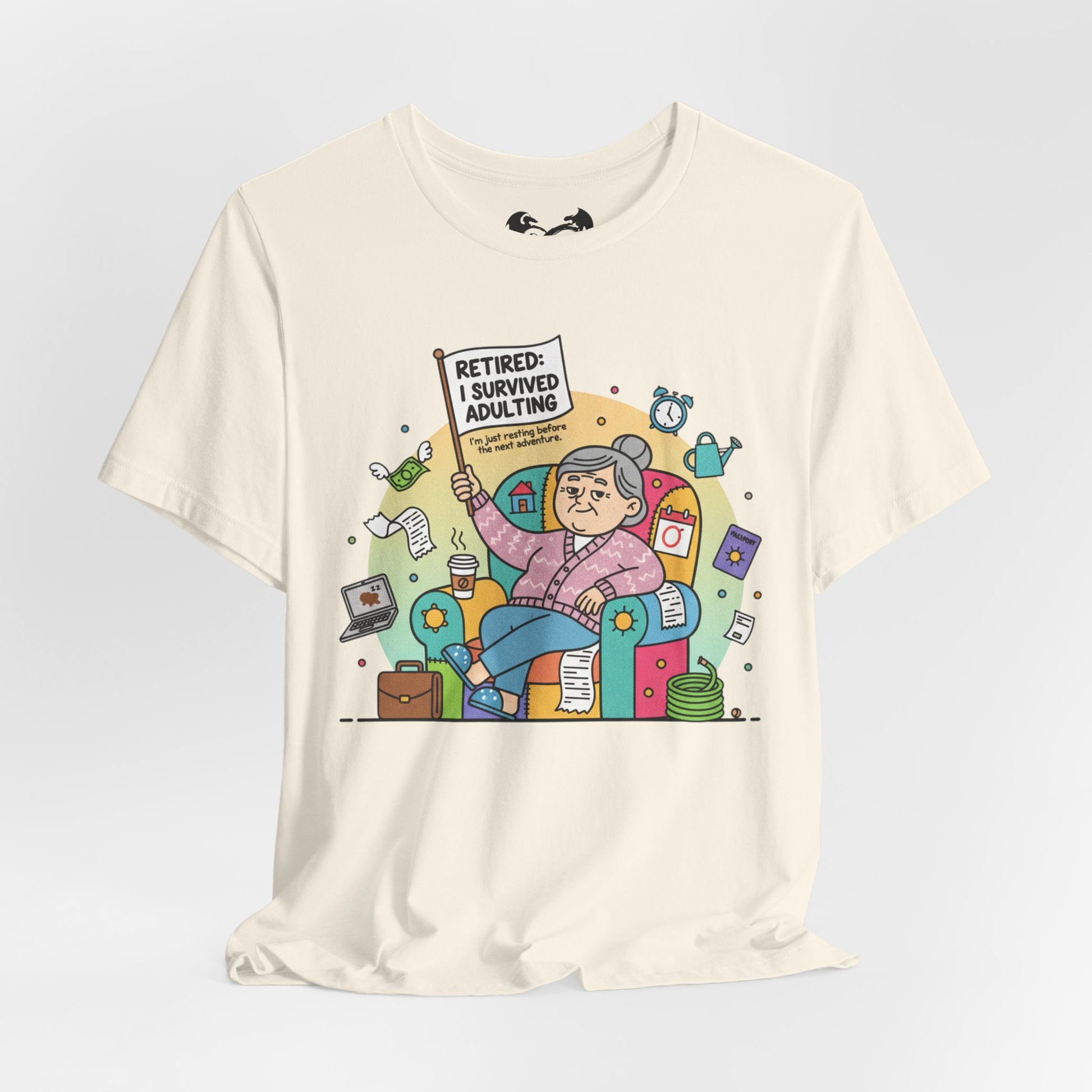 Beige t-shirt with a colorful graphic of a retired person holding a sign 'Retired: I survived adulting' on a light gray background.