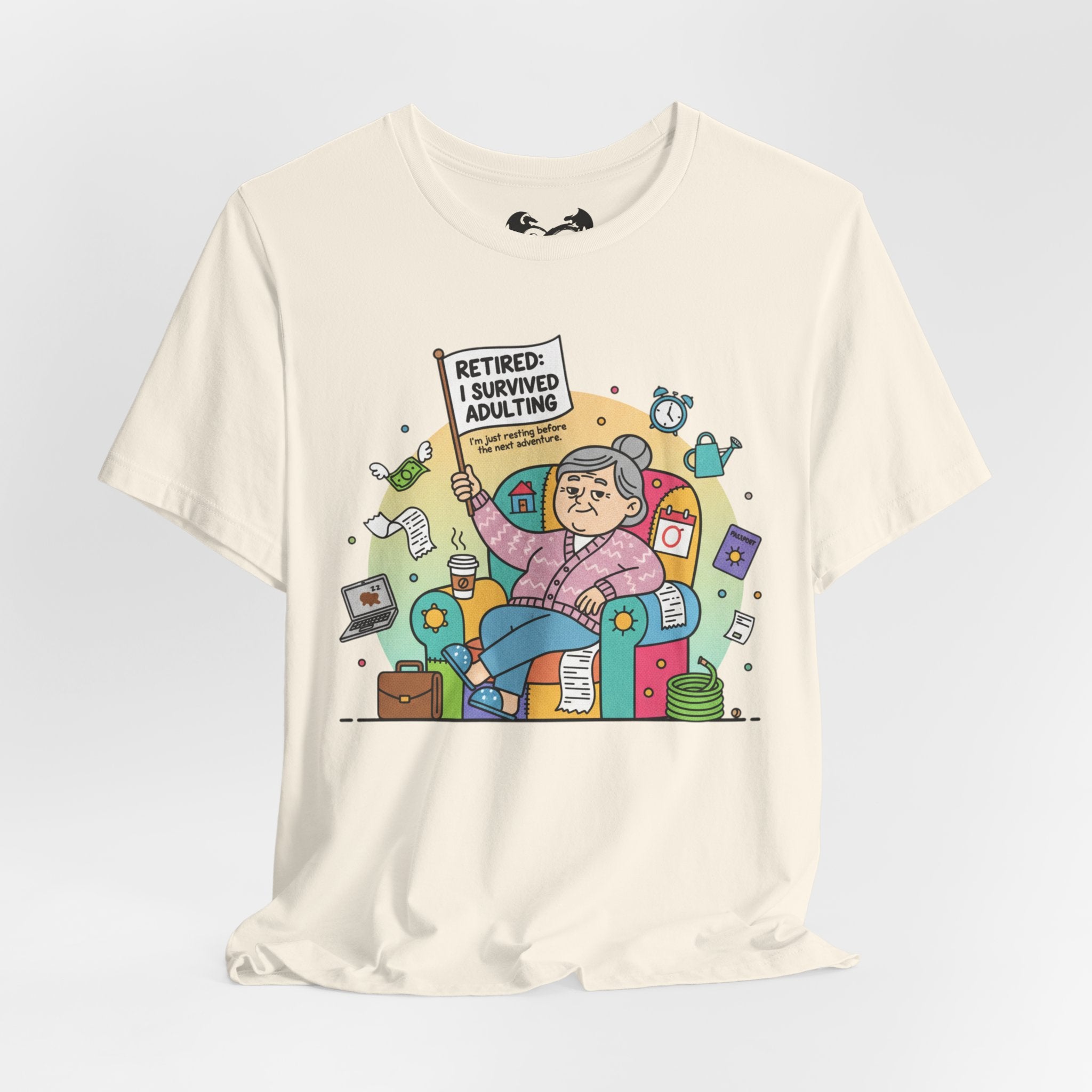 Beige t-shirt with a colorful graphic of a retired person holding a sign 'Retired: I survived adulting' on a light gray background.