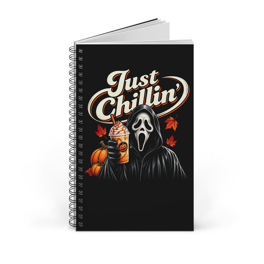 A spiral-bound notebook with a black cover featuring a Ghostface-style hooded figure in a white mask, holding a pumpkin and an iced coffee, with the words 'Just Chillin'' in large white script. The notebook is photographed on a clean white background.