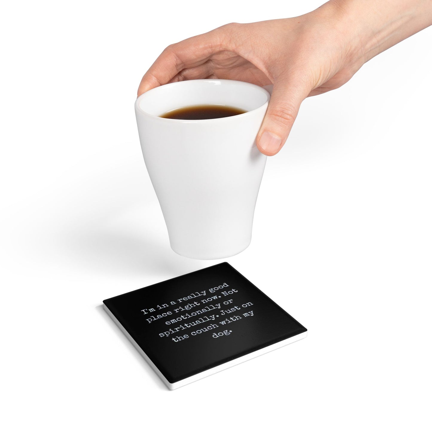 White mug with coffee on a coaster with text, hand holding the mug