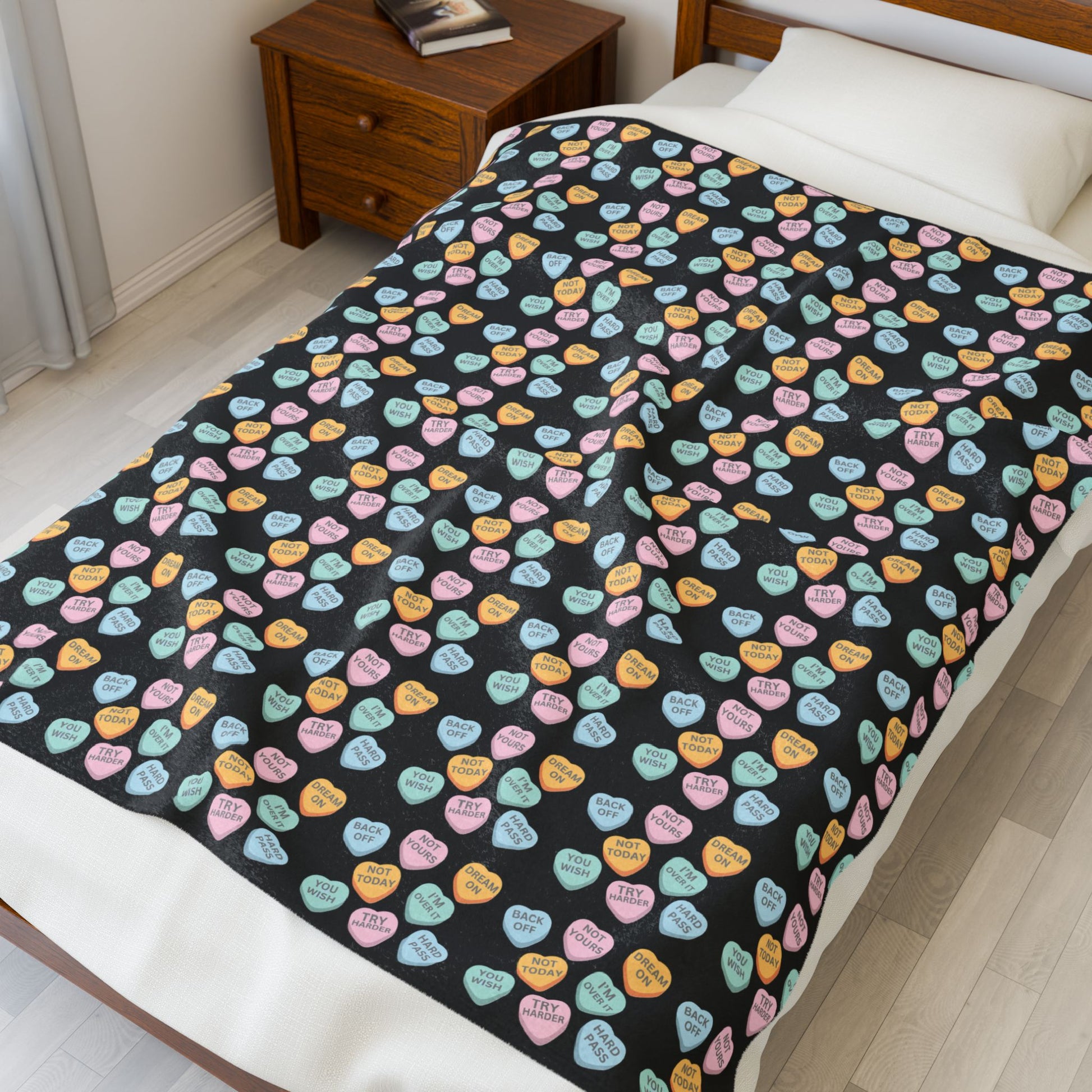 Black blanket with colorful candy hearts pattern on a bed in a bedroom.