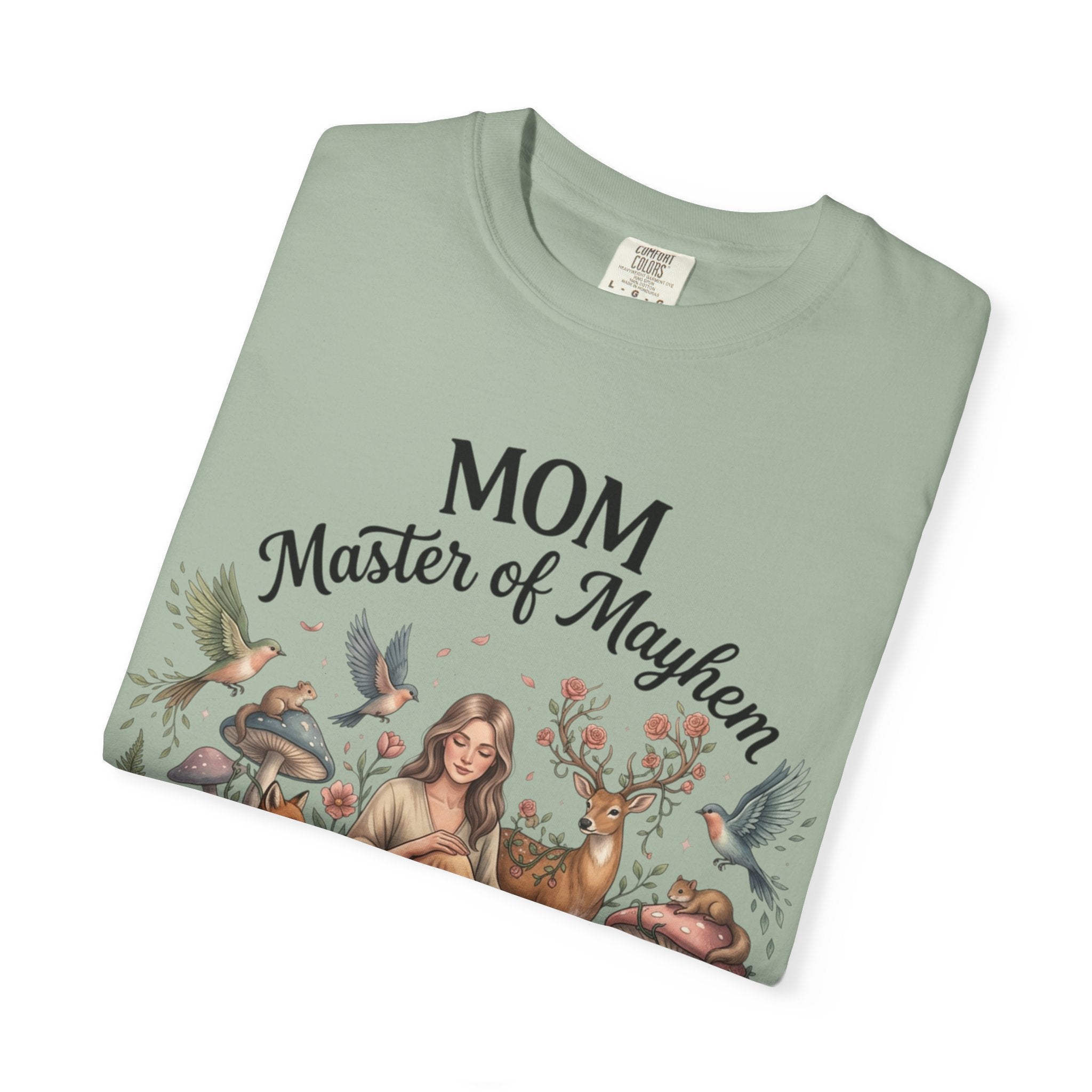 Folded light green t-shirt with 'Mom Master of Mayhem' text and nature-themed design on a white background