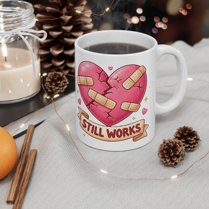 Mug with a heart design and 'Still Works' text on a table with decorative items.
