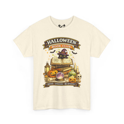 An off-white short-sleeve t-shirt with a graphic print on the front. The graphic features a witch cat wearing a purple hat next to an open book, surrounded by pumpkins, a cauldron, candles, and banners that read 'HALLOWEEN BOOK CLUB' and 'READ • DISCUSS • BE SPOOKY'.