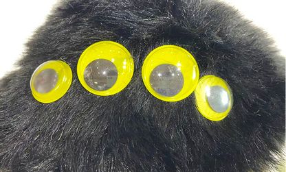 Four large, glossy yellow plastic eyes with clear reflective centers, arranged in a row on a black furry surface.