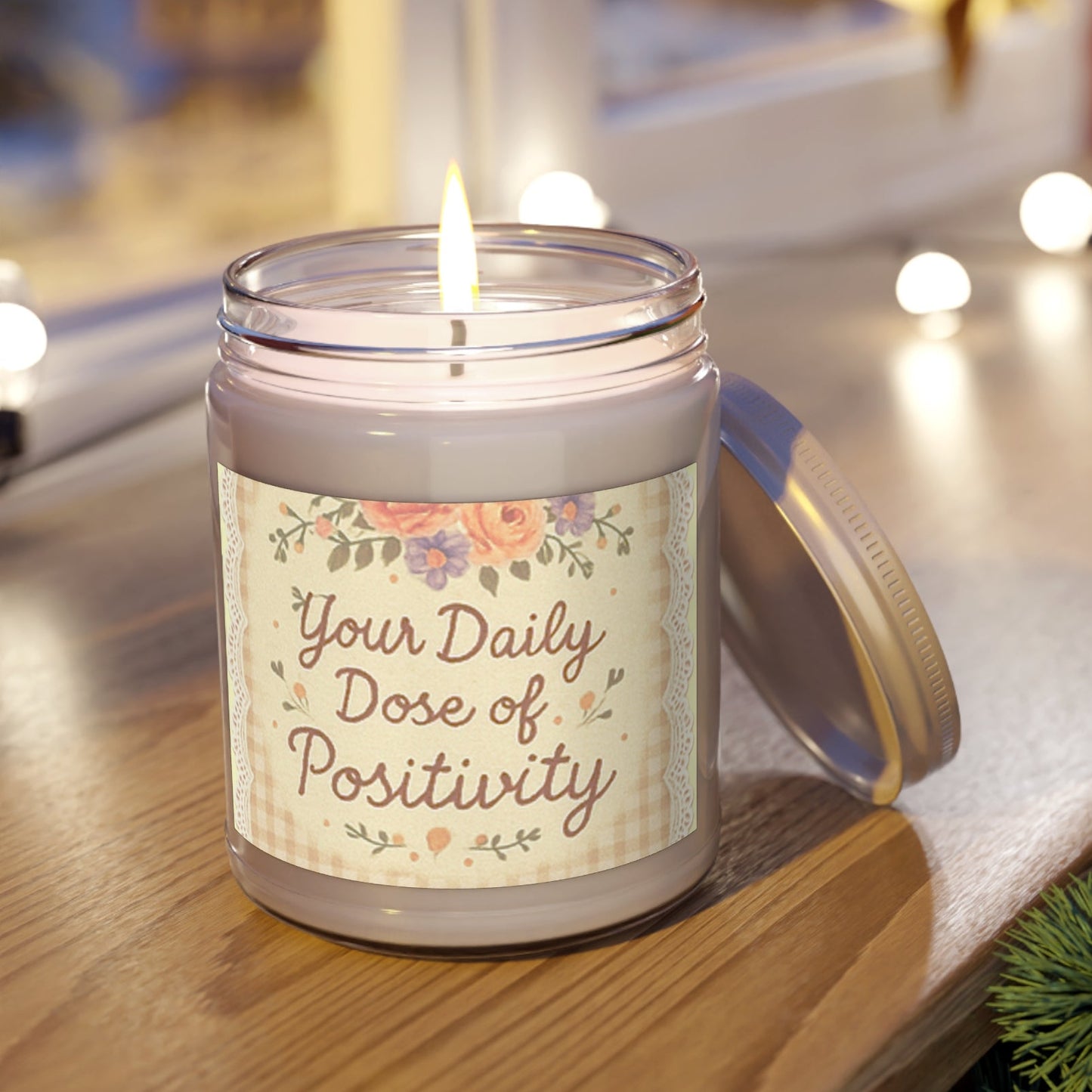 Candle in a jar with a label reading 'Your Daily Dose of Positivity' on a wooden surface.