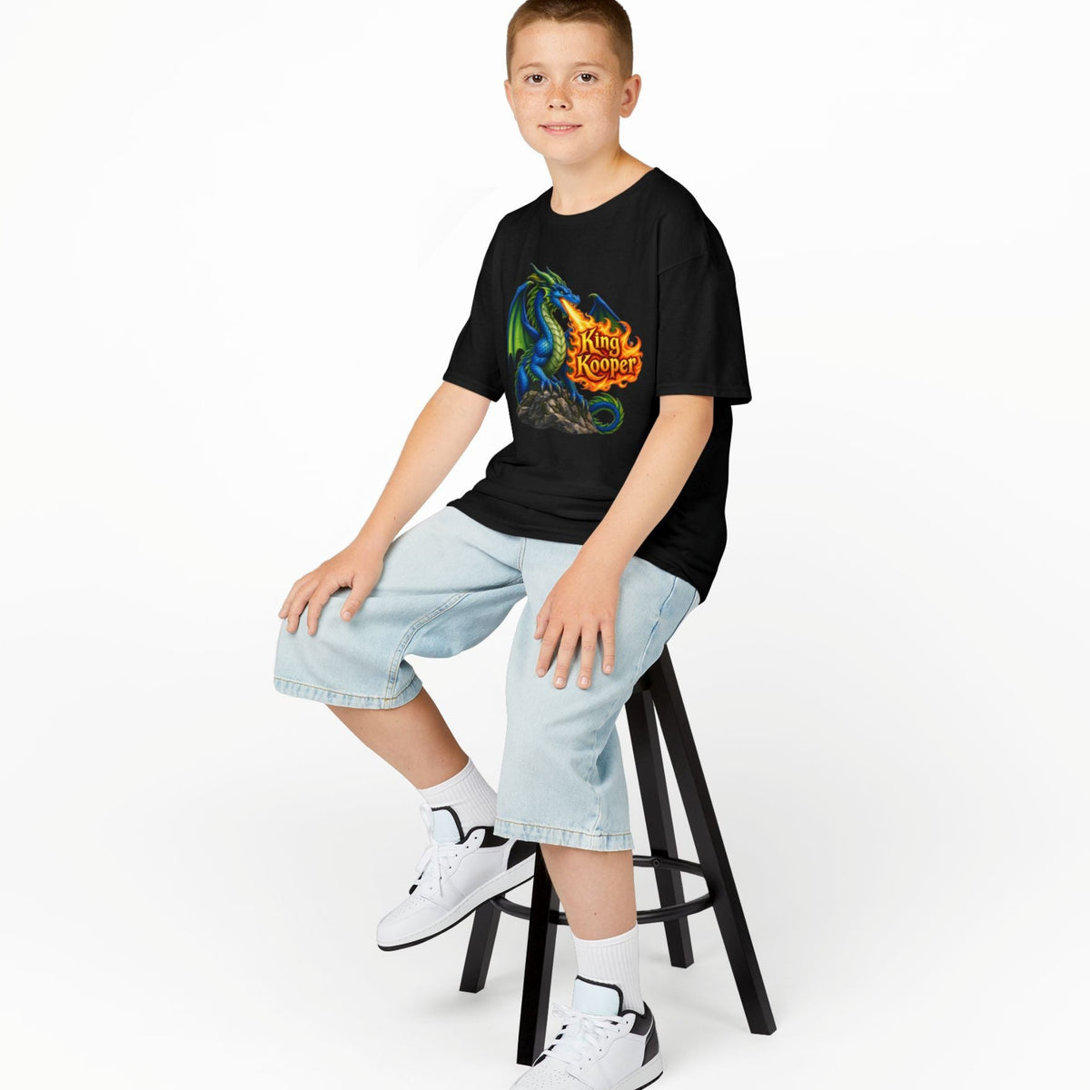 Person wearing a black t-shirt with text and graphics, sitting on a stool against a white background