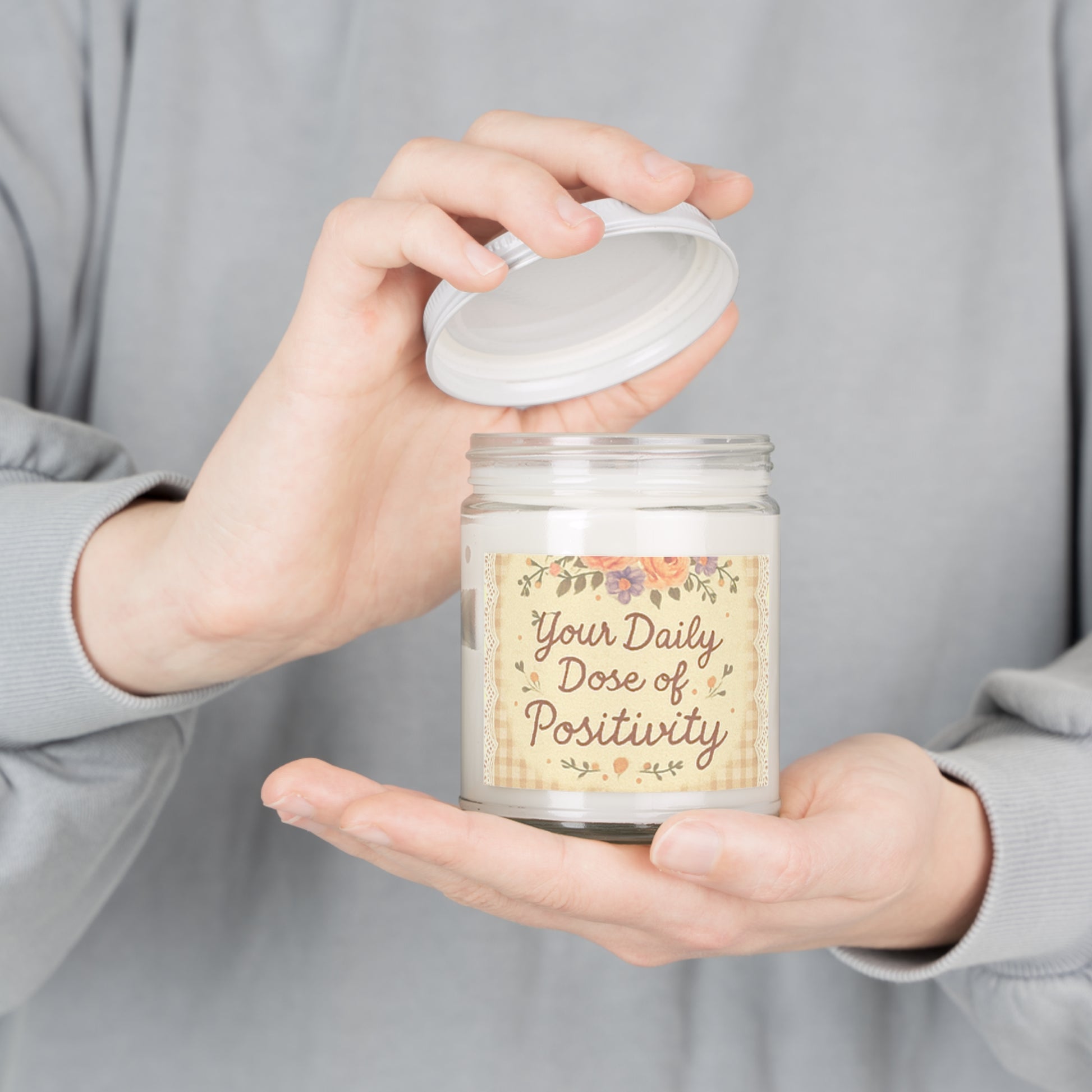 Person holding a candle labeled 'Your Daily Dose of Positivity' with a floral design.