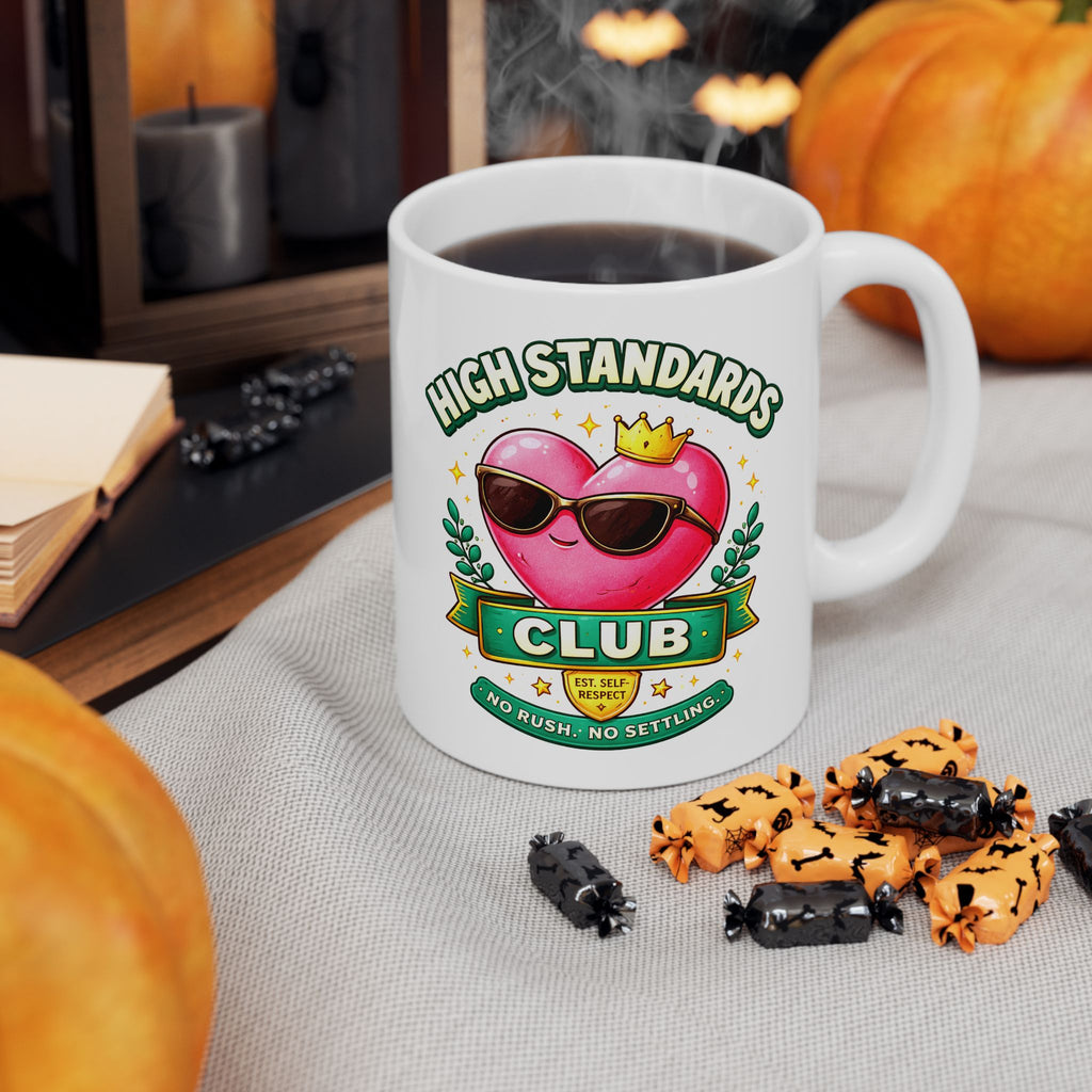 White mug with 'High Standards Club' design on a table with pumpkins and treats.