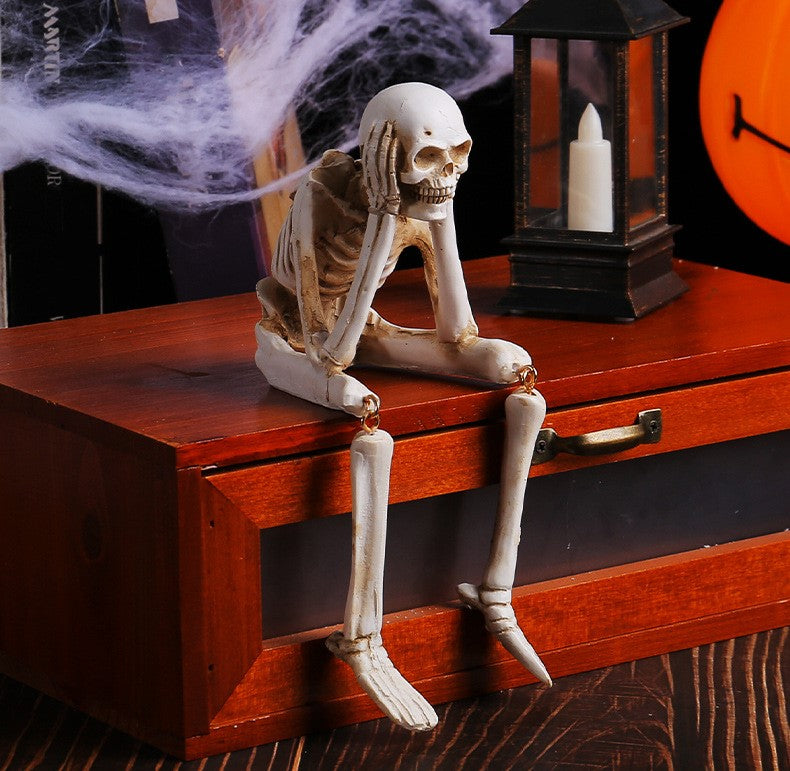 A posed skeleton figurine sitting on the edge of a reddish-brown wooden chest, with a black lantern and white candle behind it and purple smoke effects around the skull.